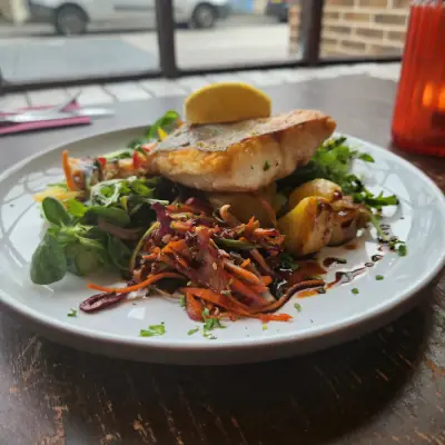 Pan-seared fish fillet with mixed salad leaves, grated vegetables, and lemon wedge served on white plate