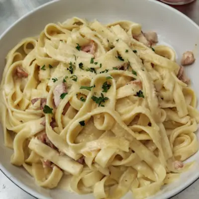 Creamy fettuccine pasta with bacon pieces and fresh herbs served in white bowl