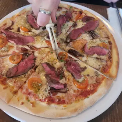 Stone-baked pizza topped with cured ham, cherry tomatoes, cheese and herbs being sliced with pizza cutter