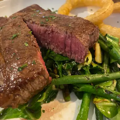 Medium-rare grilled steak sliced to show pink interior, served with green beans and chips, garnished with fresh herbs